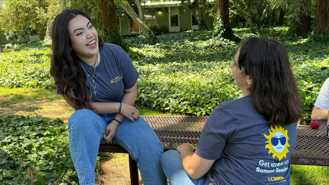 two students sitting in the courtyard on a picnic table. Both are wearing Summer Sessions t-shirts.